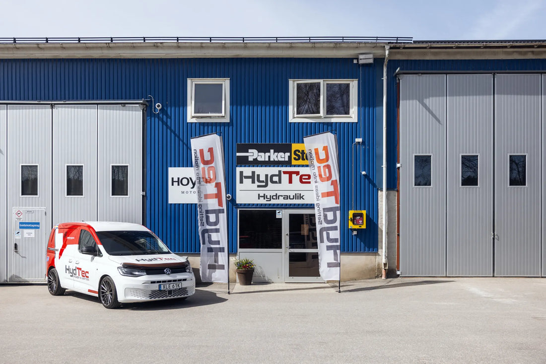 A blue industrial building with large gray garage doors, a white and red service van parked in front, and two vertical banners reading Parker Store and HydTec Hydraulics