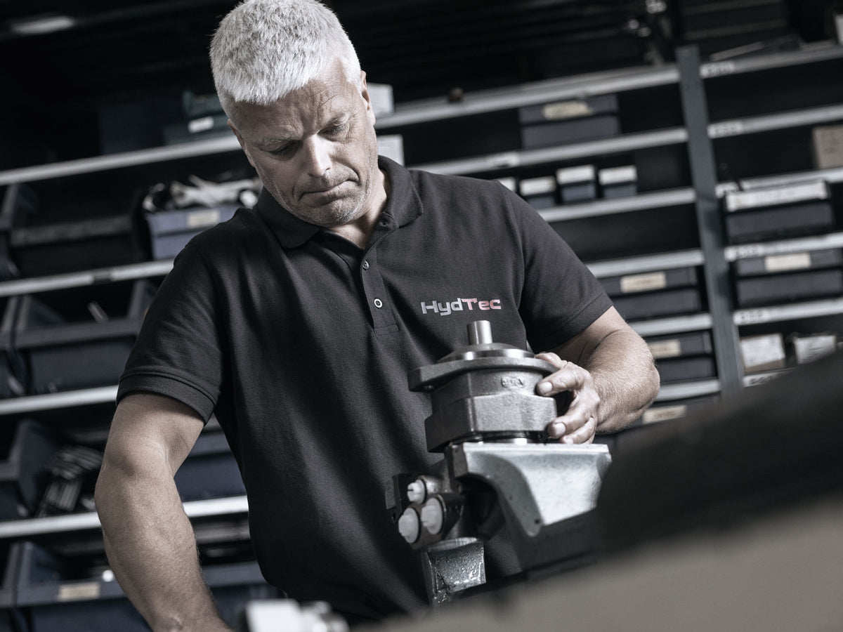 A Hyd-Tec employee working on a machine in an industrial workshop setting with shelves in the background.