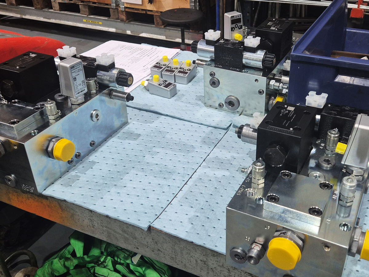 Workbench setup showing hydraulic manifold blocks alongside surface roughness testing equipment and calibration documentation.